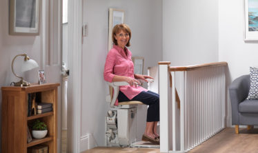 Woman on a Stannah stairlift at the top of the stairs on the first floor of the house